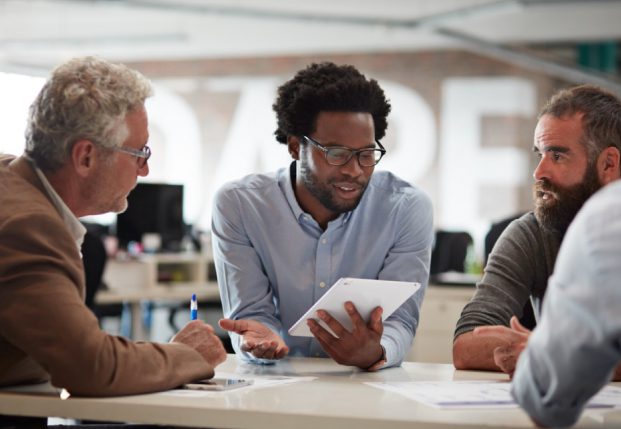 People in office working together review information on a tablet in a conference room.