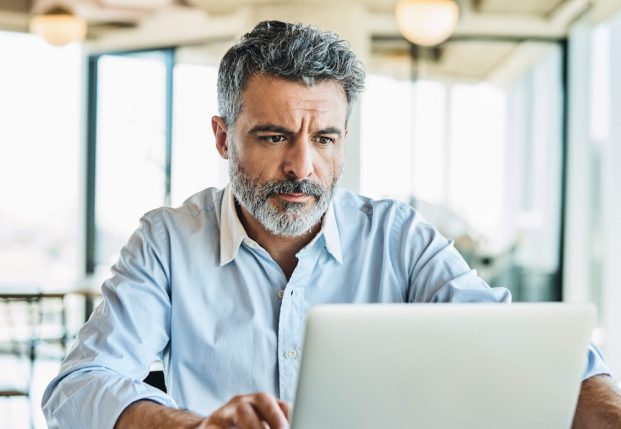 Older person in buttoned up shirt at home working on computer.