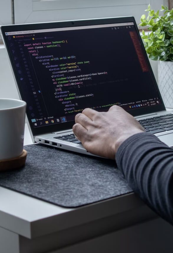 A hand rests on a laptop keyboard, which shows code on a screen